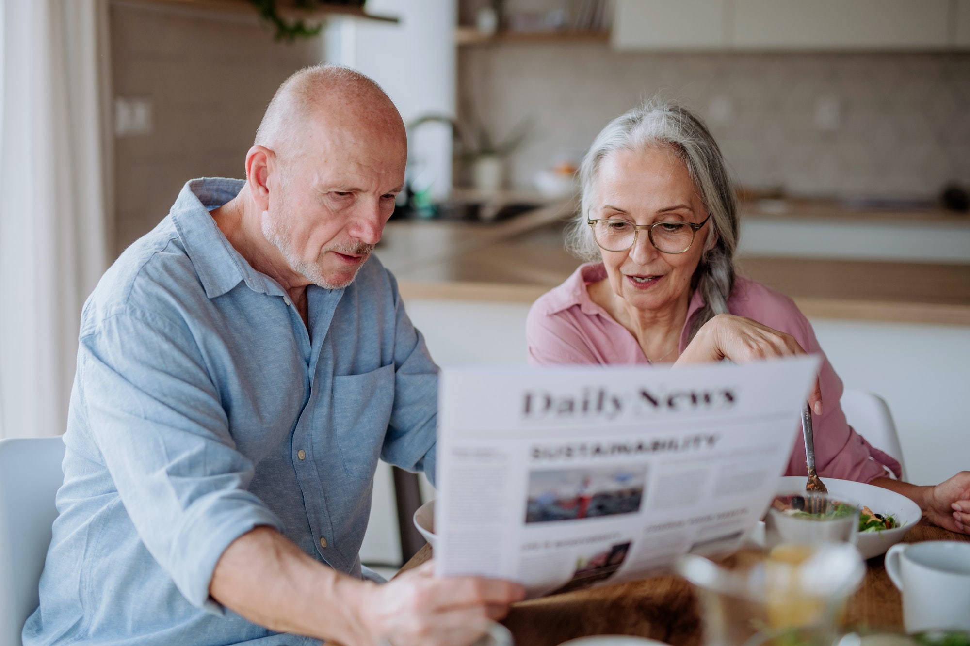 Happy senior couple having breakfast and reading newspaper together at home.